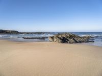 a large rock is on a beach next to the water and sand area, as if its in ocean