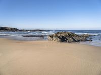 a large rock is on a beach next to the water and sand area, as if its in ocean