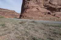 a person riding a motorcycle along a narrow road through rocks and sand cliffs a grassy area on both sides