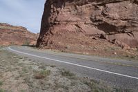 a person riding a motorcycle along a narrow road through rocks and sand cliffs a grassy area on both sides