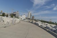 there is a rock wall lined walkway by the water's edge with a city skyline in the distance