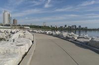 there is a rock wall lined walkway by the water's edge with a city skyline in the distance