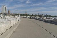 there is a rock wall lined walkway by the water's edge with a city skyline in the distance