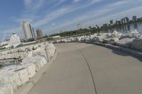 there is a rock wall lined walkway by the water's edge with a city skyline in the distance