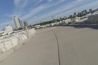 there is a rock wall lined walkway by the water's edge with a city skyline in the distance