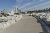 there is a rock wall lined walkway by the water's edge with a city skyline in the distance