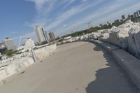 there is a rock wall lined walkway by the water's edge with a city skyline in the distance