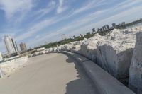 there is a rock wall lined walkway by the water's edge with a city skyline in the distance