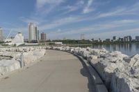 there is a rock wall lined walkway by the water's edge with a city skyline in the distance