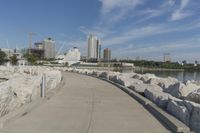 there is a rock wall lined walkway by the water's edge with a city skyline in the distance