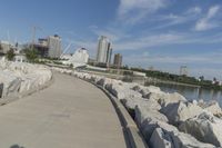 there is a rock wall lined walkway by the water's edge with a city skyline in the distance