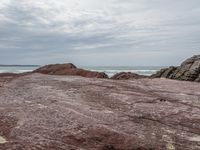 a man stands at the edge of a rocky beach while standing on red sand and looking out into the ocean
