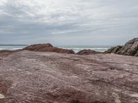 a man stands at the edge of a rocky beach while standing on red sand and looking out into the ocean