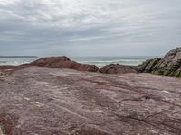 a man stands at the edge of a rocky beach while standing on red sand and looking out into the ocean