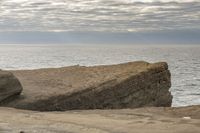 a person sitting on a rock in front of the ocean on a cloudy day by the water