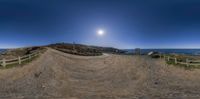 a dirt bike ramp is on the rocky beach beside the ocean with a beautiful full moon in the blue sky