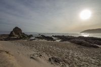 the sun is setting over the sea near rocky beachfronts with several sand castles