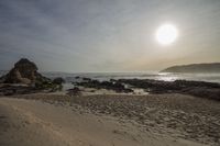 the sun is setting over the sea near rocky beachfronts with several sand castles