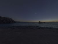 a picture of a rocky coast at dusk with stars and the sun setting in the background