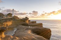 a rocky area with a lighthouse in the distance and a person on a small boat in the distance