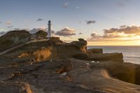 a rocky area with a lighthouse in the distance and a person on a small boat in the distance