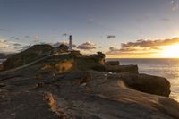 a rocky area with a lighthouse in the distance and a person on a small boat in the distance