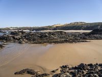 a sandy beach with large rocks and water near the shore of a bay on a sunny day