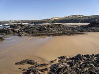 a sandy beach with large rocks and water near the shore of a bay on a sunny day