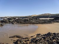 a sandy beach with large rocks and water near the shore of a bay on a sunny day