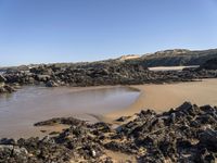 a sandy beach with large rocks and water near the shore of a bay on a sunny day