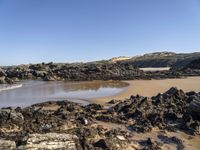 a sandy beach with large rocks and water near the shore of a bay on a sunny day