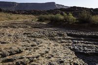 the road is full of rocks and bushes on the side of the desert with mountains in the background