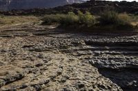 the road is full of rocks and bushes on the side of the desert with mountains in the background