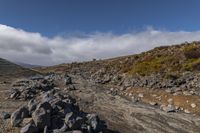 there is a small rocky field that is full of rocks and gravel near mountains under a cloudy blue sky