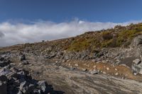 there is a small rocky field that is full of rocks and gravel near mountains under a cloudy blue sky