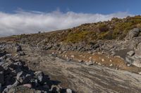 there is a small rocky field that is full of rocks and gravel near mountains under a cloudy blue sky