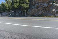 a rocky hill near a road and tree lined path with no traffic in it and no right lane