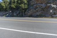 a rocky hill near a road and tree lined path with no traffic in it and no right lane