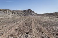 a dirt road through an empty field in a mountainous area with rocky hills on both sides