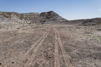 a dirt road through an empty field in a mountainous area with rocky hills on both sides