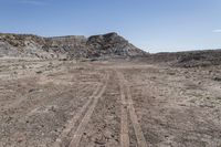 a dirt road through an empty field in a mountainous area with rocky hills on both sides