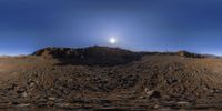 a man is on top of some rocky hills under a bright moon lit sky and in the distance, there are some mountains