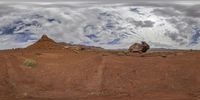 a large rock sits in the dirt with a sky background and clouds overhead for a shot