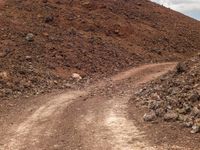 a small truck sits on a dirt road in front of a rocky mountain with a dirt slope