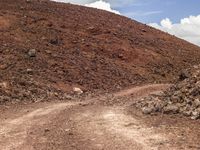 a small truck sits on a dirt road in front of a rocky mountain with a dirt slope