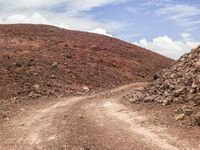 a small truck sits on a dirt road in front of a rocky mountain with a dirt slope