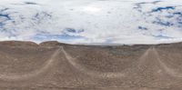 a cloudy sky is above a rocky mountain side landscape as seen through a 360 camera lens