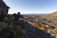 rocky terrain with rocks and shrubs along a hill on the edge of a cliff with mountains in the background