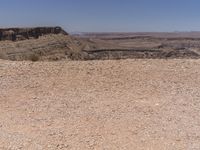 a man rides his bike along a rocky terrain trail, a vast desert plain in the distance