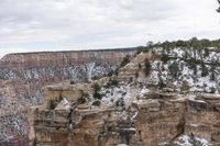 a rocky cliff covered in snow in the mountains near an area with trees and cliffs